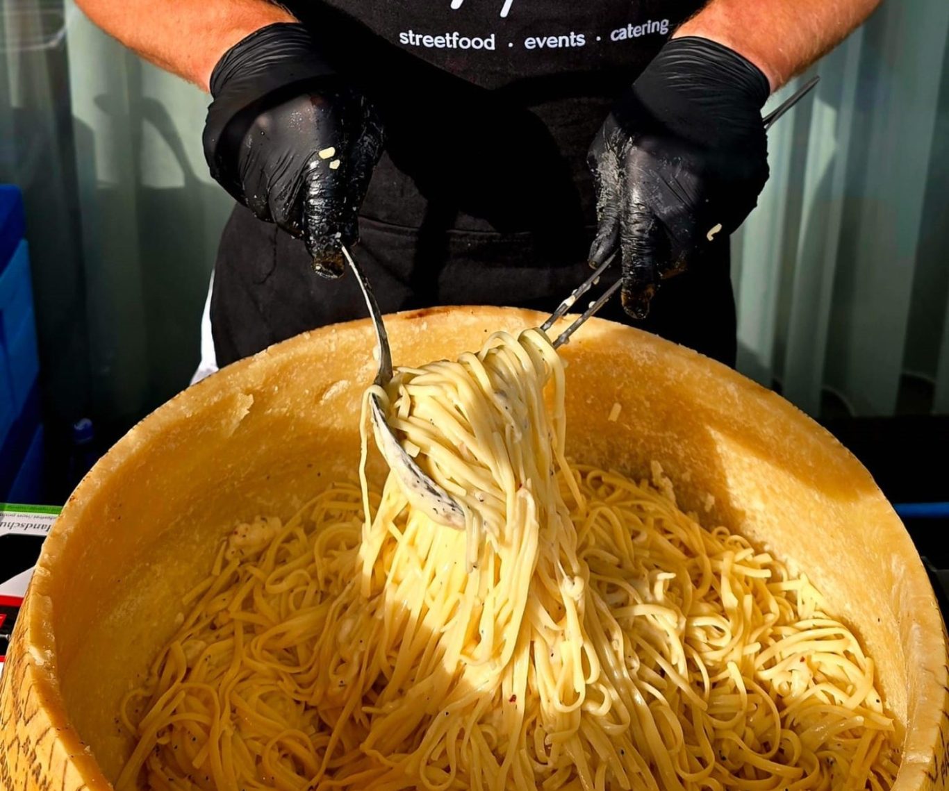 Live-Cooking: Eine Person hebt frische Spaghetti aus einem großen Parmesanlaib. 